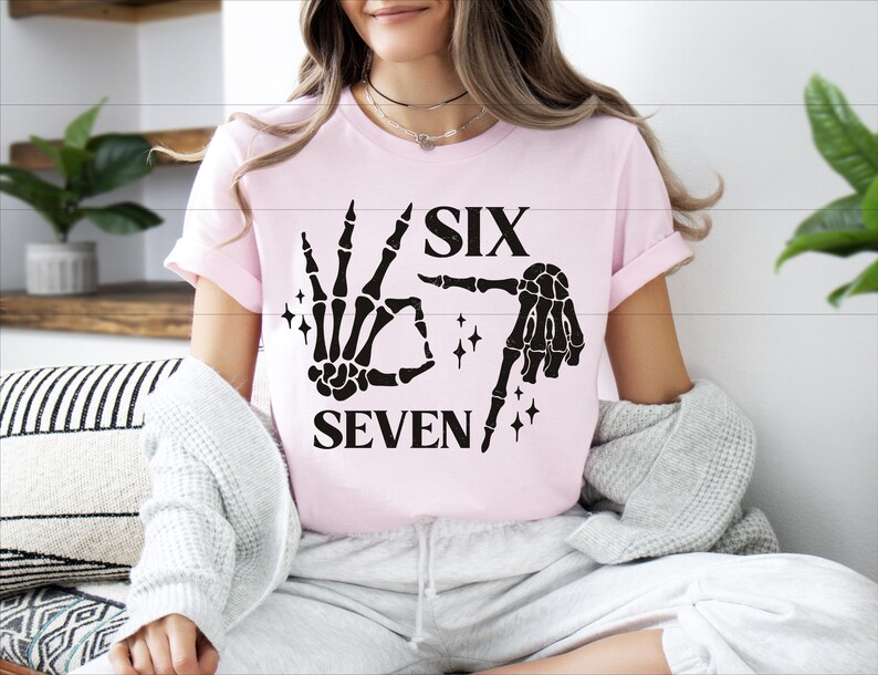 A woman wearing a pink t-shirt with a graphic design of a skeleton hand and the text "SIX SEVEN" is sitting on a couch.