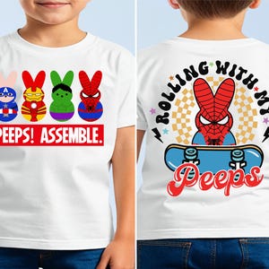 May include: White t-shirt with a graphic of four superhero Peeps characters on the front. The back of the shirt has a graphic of a Spiderman Peep on a skateboard with the text "Rolling with my Peeps!"