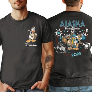 A man wearing a black t-shirt with a graphic design featuring Disney characters and text related to Alaska.