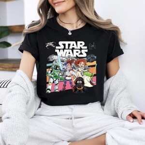 A woman wearing a black t-shirt with a Star Wars graphic design, sitting on a couch with a white blanket draped over her.