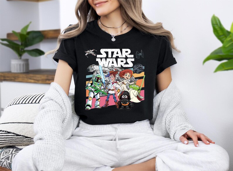 A woman wearing a black t-shirt with a Star Wars graphic design, sitting on a couch with a white blanket draped over her.