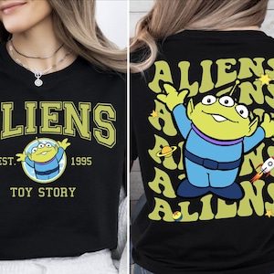 Puede incluir: Camiseta negra con un personaje extraterrestre verde de Toy Story. La parte delantera de la camiseta dice "Aliens Est. 1995 Toy Story". La parte trasera de la camiseta tiene un patr&oacute;n repetido de la palabra "Aliens" con el personaje extraterrestre en el centro.