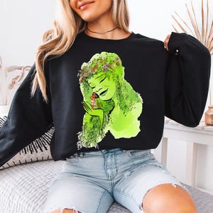 a woman sitting on a bed wearing a black shirt with a picture of a woman