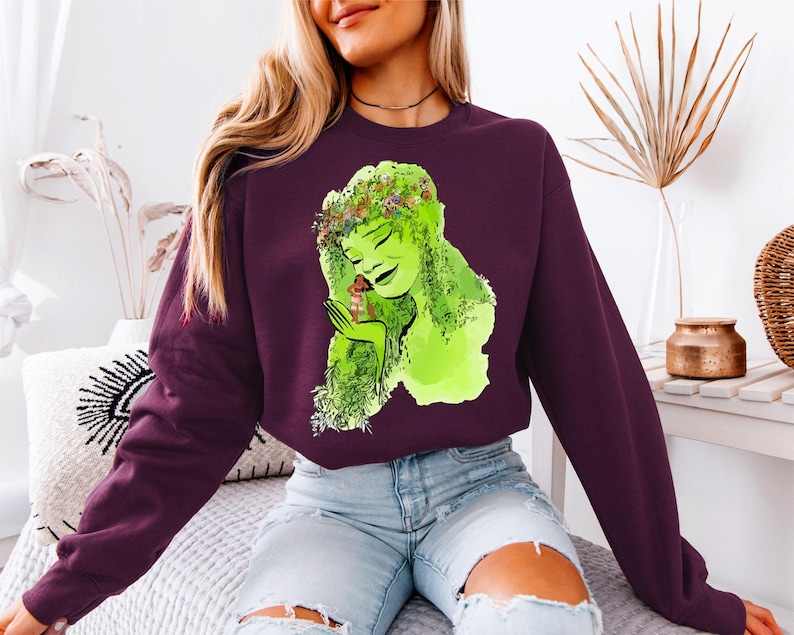 a woman sitting on a bed wearing a purple shirt with a green woman on it