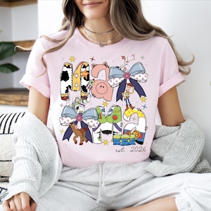 A woman wearing a pink t-shirt with a colorful graphic design featuring cartoon characters and text.