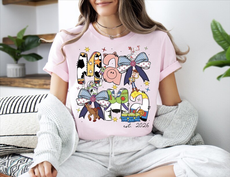 A woman wearing a pink t-shirt with a colorful graphic design featuring cartoon characters and text.