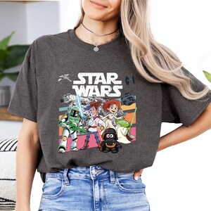 A woman wearing a gray t-shirt with a Star Wars graphic and cartoon characters, including a character holding a sword and a character with a green hat.