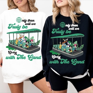 Könnte beinhalten: Weiße und schwarze Sweatshirts mit einem grünen grafischen Aufdruck einer Bootsfahrt mit Mickey Mouse und seinen Freunden. Der Text auf den Sweatshirts lautet "Only then will we truly be living with the land".