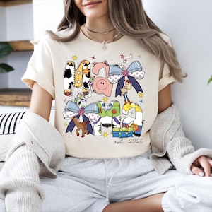 A woman wearing a t-shirt with a cartoon character design and text, sitting on a couch with plants in the background.