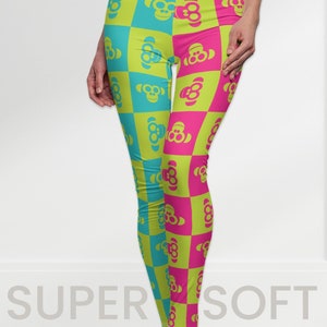 Puede incluir: Leggings con un patrón de tablero de ajedrez en verde neón, turquesa y rosa. Cada cuadrado presenta un diseño de cara de mono. El texto "SUPER SOFT" es visible en la parte inferior. Estos leggings son una adición vibrante y lúdica.