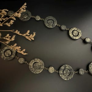 May include: A black necklace with large, round, textured pendants connected by a thin gold chain.