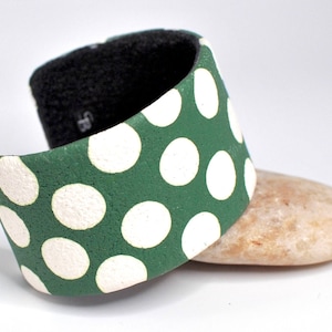 May include: A green and white polka dot bracelet made of fabric. The bracelet is wide and has a slightly rounded shape.