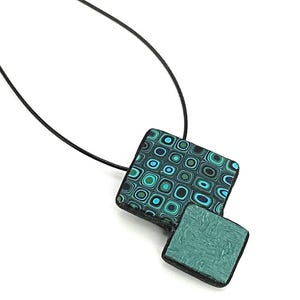 May include: A teal and black geometric patterned pendant necklace with a black cord.