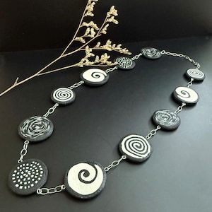 May include: A black and white necklace with round pendants featuring different swirling patterns. The necklace is made of a silver chain.