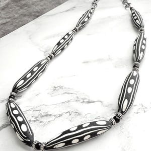 May include: A black and white patterned necklace with silver chain and black beads. The necklace features long, oval-shaped beads with a white and black striped pattern.