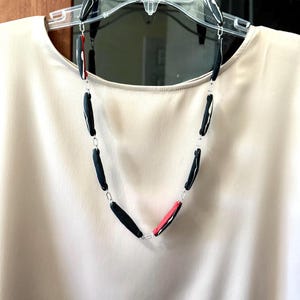 May include: A black and red necklace with white accents. The necklace is made of small, rectangular beads connected by a silver chain.