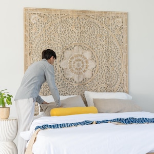 Puede incluir: Una cabecera de cama de madera blanca con tallas intrincadas, una cama blanca con una almohada de apoyo amarilla y una manta de tiro con estampado azul y blanco.