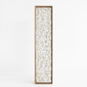 May include: White wooden wall decor with a carved floral design. The design is intricate and detailed, with a light brown wood frame.