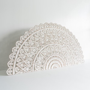 May include: White, semi-circular, carved wooden wall decor. The intricate design features floral and geometric patterns, creating a detailed, openwork appearance. The piece is painted white and has a distressed finish. This decorative item is suitable for home decor.