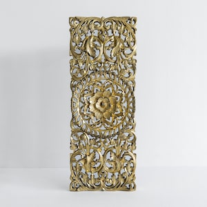 May include: A gold-colored wooden wall decor panel with intricate floral carvings. The panel is rectangular and features a central circular design with a flower motif.