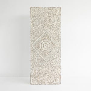 Puede incluir: Panel rectangular de madera blanquecina tallado con intrincados patrones florales y de volutas. Un diseño central en forma de diamante muestra un motivo floral detallado, agregando profundidad e interés visual.