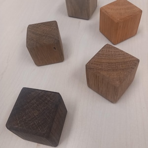 Könnte beinhalten: Fünf Holzquader in verschiedenen Braun- und Beigetönen sind auf einer hellen Oberfläche angeordnet. Die Quader haben eine geometrische Form mit sichtbarer Holzmaserung, die natürliche Farb- und Texturvariationen zeigt. Die Quader sind eine Mischung aus hellen und dunklen Tönen.