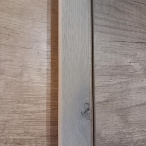 Peut inclure: Une moulure en bois de couleur claire, peut-être pour le revêtement de sol ou un projet de construction similaire, est présentée contre une surface à grain de bois. La garniture présente un nœud et quelques imperfections. Le grain du bois est visible.