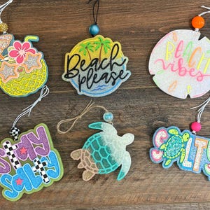 May include: Six decorative hanging ornaments featuring beach themes. Designs include a pineapple with sunglasses, a circular sign with palm trees and the text Beach please, a round sign with Beach vibes, Stay salty text, a sea turtle, and a Salty sign.
