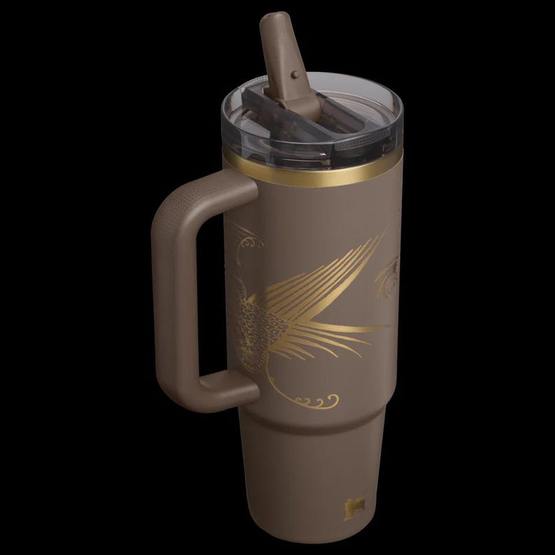 Puede incluir: Un vaso t&eacute;rmico marr&oacute;n con asa y pajita. El vaso presenta un dise&ntilde;o de p&aacute;jaro dorado y una banda dorada alrededor de la parte superior. La tapa es transparente con un cierre abatible marr&oacute;n. Tiene una capacidad aproximada de 887 ml.