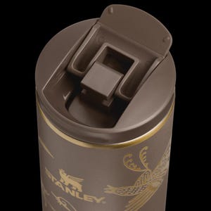 Puede incluir: Taza de viaje Stanley marr&oacute;n con tapa abatible. La taza presenta elementos decorativos dorados y el logotipo de Stanley. La tapa est&aacute; abierta, revelando el interior. La taza est&aacute; dise&ntilde;ada para bebidas fr&iacute;as o calientes.
