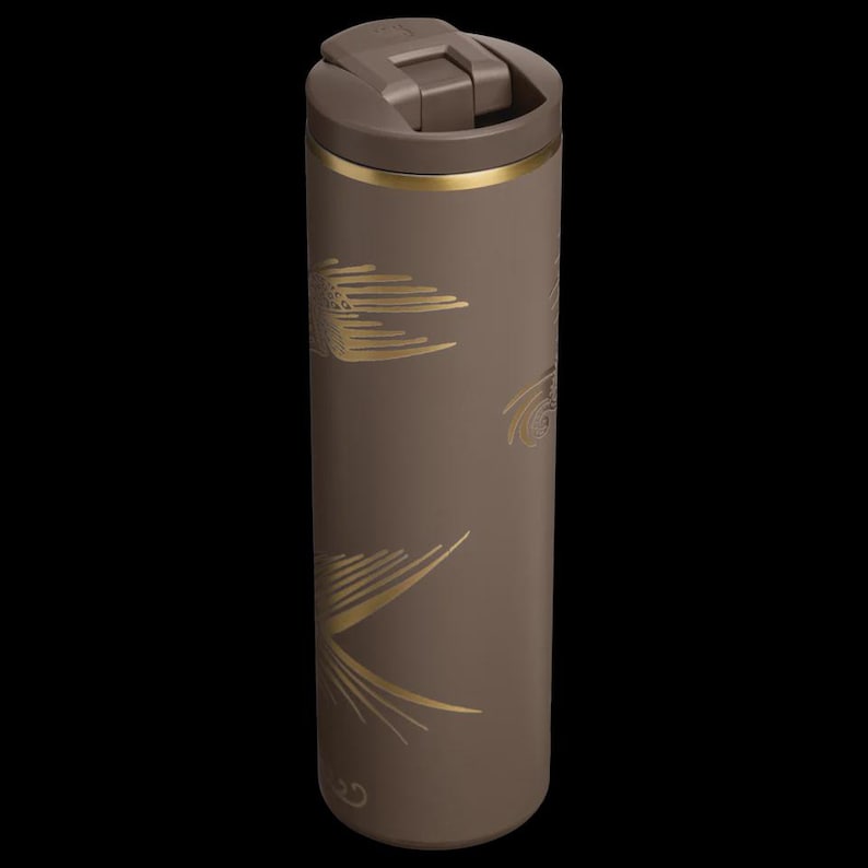 Puede incluir: Un termo de viaje marr&oacute;n con una banda dorada y un dise&ntilde;o de hojas doradas. El termo tiene una tapa abatible y es de forma cil&iacute;ndrica. El termo mide unos 20 cm de alto.