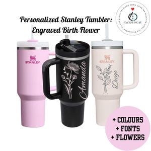 May include: Three Stanley tumblers in pink, black, and cream, each with a handle and straw. The pink tumbler has the Stanley logo. The black tumbler is engraved with a floral design and the name "Amanda." The cream tumbler has a floral design and the name "Diego."