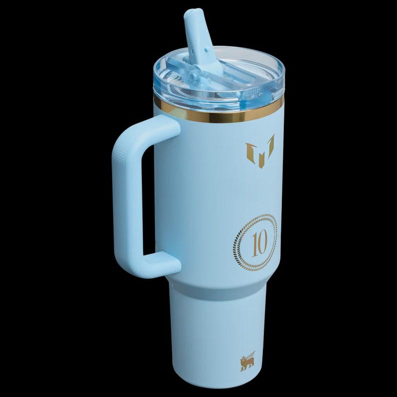 May include: A light blue insulated tumbler with a handle, a clear lid, and a straw. The tumbler has gold accents and a gold "10" graphic. A gold logo is at the bottom. The tumbler is designed to hold approximately 40 ounces.