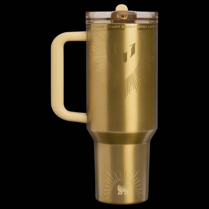 May include: A gold-colored insulated tumbler with a cream-colored handle and lid. The tumbler features an engraved design of a shield with sunburst rays and the text "START EARLY STAY LATE". A lion emblem is at the bottom.