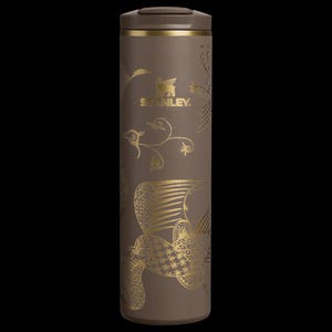 Puede incluir: Un termo de viaje Stanley marr&oacute;n con dise&ntilde;os dorados de p&aacute;jaros y flores. El termo tiene una tapa marr&oacute;n y una banda dorada en la parte superior. El logotipo de Stanley es visible en la parte delantera.