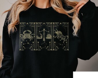 May include: Black sweatshirt with a gold design of zodiac signs, including Cancer, Libra, and Taurus.