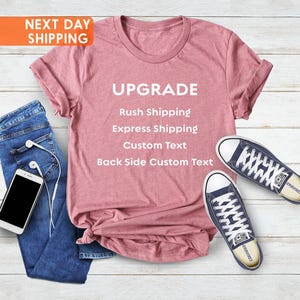 Può includere: Una t-shirt rosa polvere con testo bianco che recita UPGRADE, Rush Shipping, Express Shipping, Custom Text, Back Side Custom Text, abbinata a jeans blu, uno smartphone bianco con auricolari a filo bianchi e due scarpe di tela blu navy.