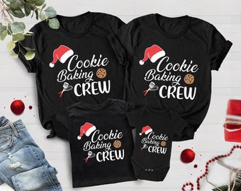 Pode incluir: Um conjunto de quatro t-shirts pretas com um tema de cozedura de biscoitos de Natal. As t-shirts apresentam um chapéu de Pai Natal vermelho, as palavras "Cookie Baking Crew" e um gráfico de biscoitos. As t-shirts estão disponíveis em tamanhos para adultos e crianças.