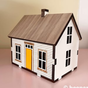 May include: A white wooden model house with a brown wood roof and a yellow door. The house has windows on the front and sides.