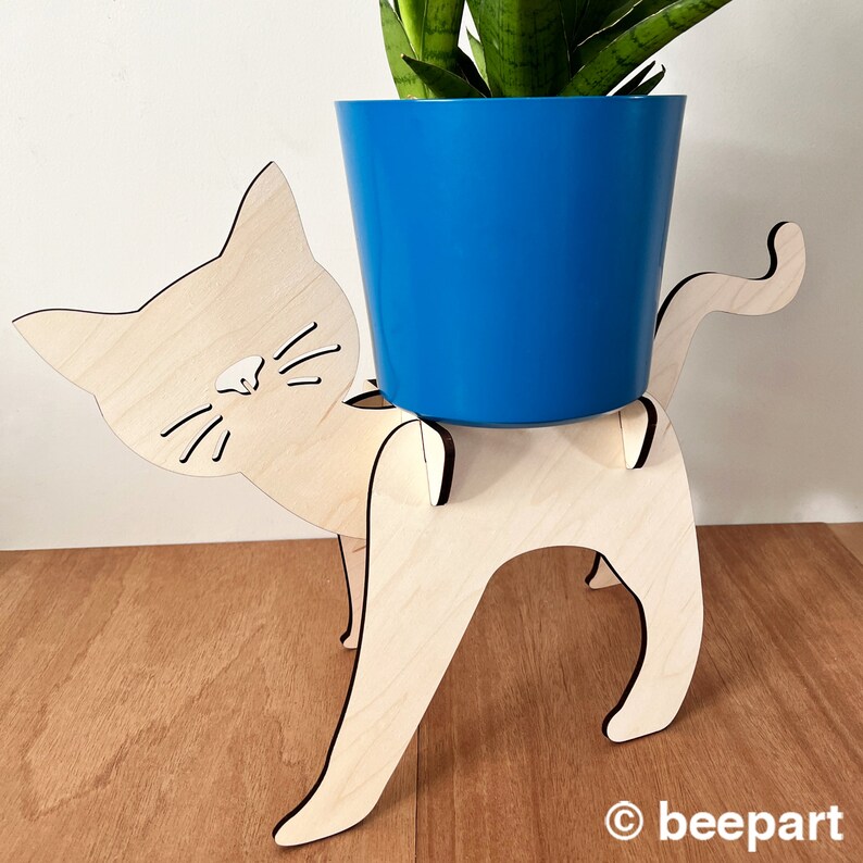 May include: A wooden cat planter stand with a blue planter pot. The cat planter stand is made of light wood and has a cute cat face design.