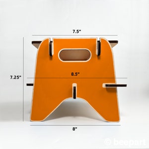 May include: Orange wooden step stool with a cutout handle. The stool measures 7.5 inches wide, 8 inches deep, and 7.25 inches tall.
