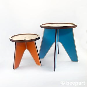 K&ouml;nnte beinhalten: Zwei Holzhocker, einer orange und einer blau, mit einem einfachen Design. Die Hocker sind aus Sperrholz und haben eine abgerundete Oberseite.