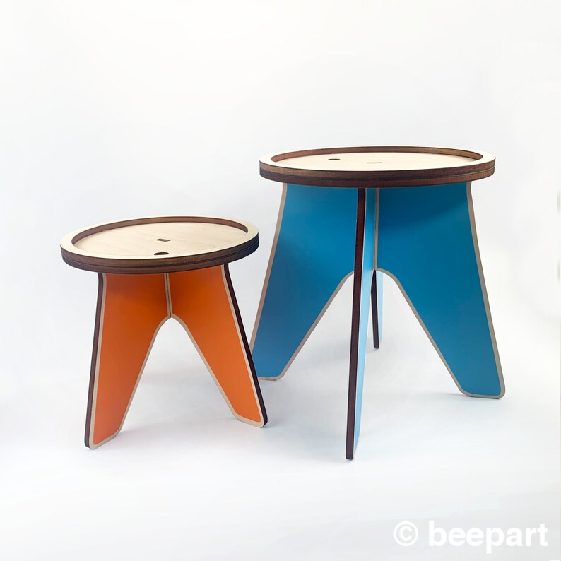 K&ouml;nnte beinhalten: Zwei Holzhocker, einer orange und einer blau, mit einem einfachen Design. Die Hocker sind aus Sperrholz und haben eine abgerundete Oberseite.