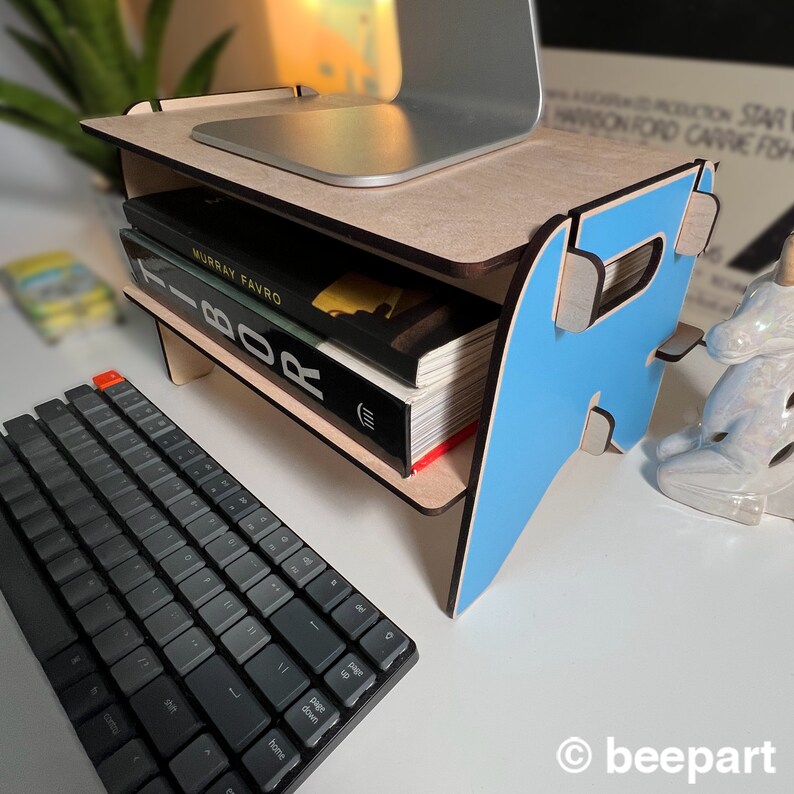 May include: A light blue wooden laptop stand with two shelves. The top shelf is holding a laptop and the bottom shelf is holding a stack of books. The stand is sitting on a white desk with a black keyboard.