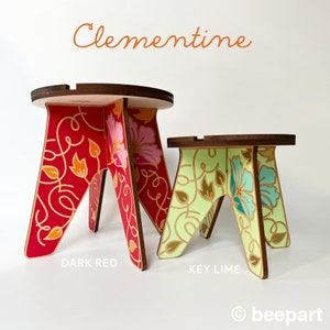 May include: Two wooden stools with floral designs. The larger stool is dark red with pink and orange flowers. The smaller stool is key lime green with blue and white flowers. The stools are labeled "DARK RED" and "KEY LIME" and the word "Clementine" is at the top of the image.