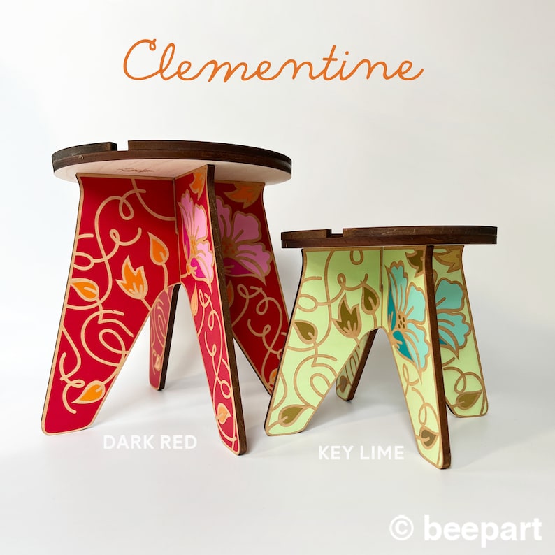 May include: Two wooden stools with floral designs. The larger stool is dark red with pink and orange flowers. The smaller stool is key lime green with blue and white flowers. The stools are labeled "DARK RED" and "KEY LIME" and the word "Clementine" is at the top of the image.