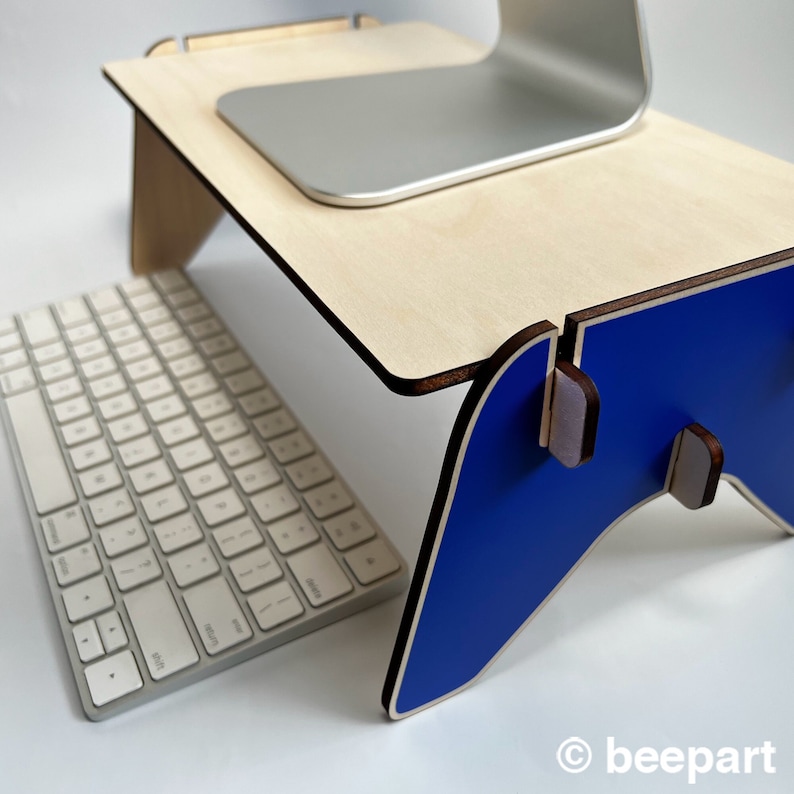 May include: A wooden laptop stand with a blue base. The stand is designed to elevate a laptop to a more ergonomic height. A white keyboard is sitting on the table in front of the stand.