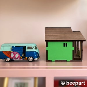 May include: A blue and white toy van with a colorful design parked next to a small wooden house with a green wall and a brown roof.