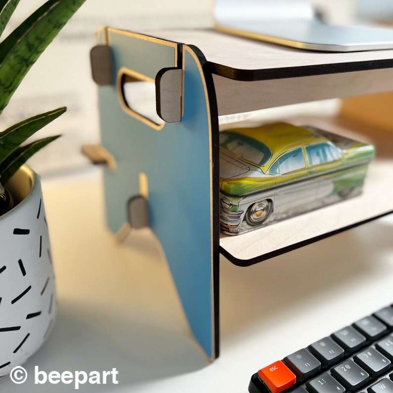 May include: A blue and wood laptop stand with two shelves. The top shelf is empty and the bottom shelf has a vintage car tin on it.