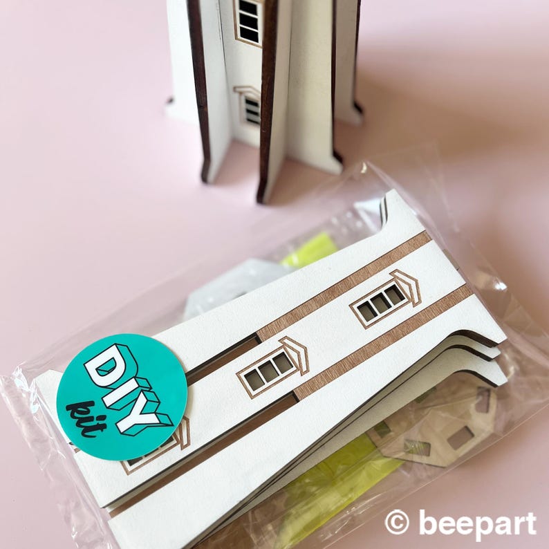 May include: A DIY kit for a wooden lighthouse model. The kit includes pre-cut wooden pieces with brown trim and window details, packaged in a clear plastic bag. A green sticker with "DIY kit" is visible. The lighthouse model is white.